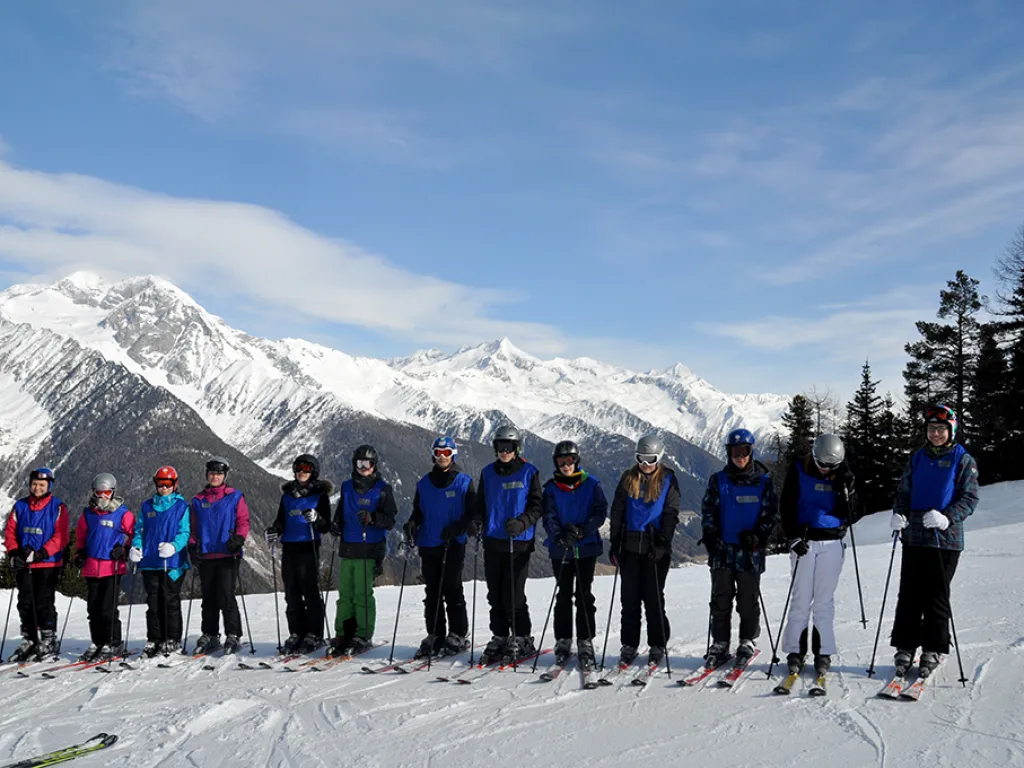 Skigruppe steht in einer Reihe vor verschneiten Gipfeln.